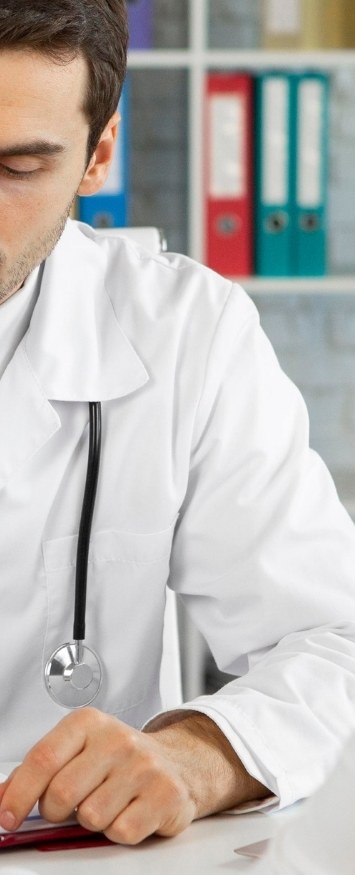 A clinician in a white coat and stethoscope working at a desk