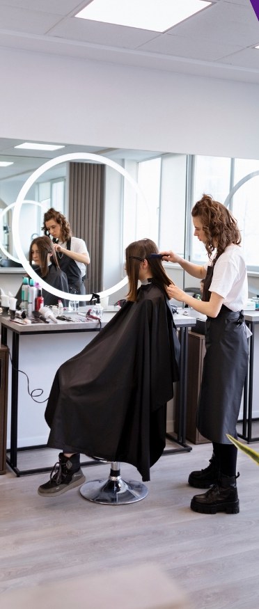 A hairdresser working on a client under ring-light mirrors in a salon